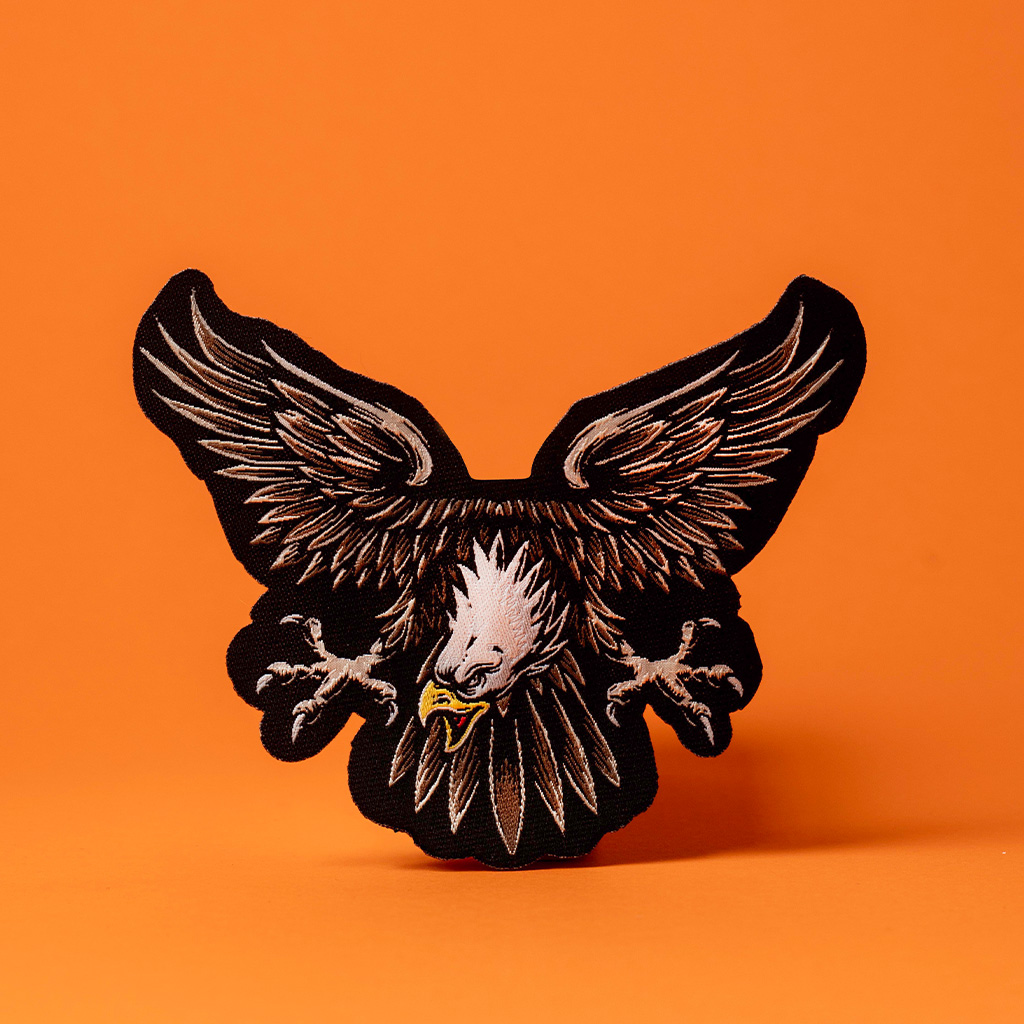 Patch brodé en forme d'aigle noir et marron sur fond orange.