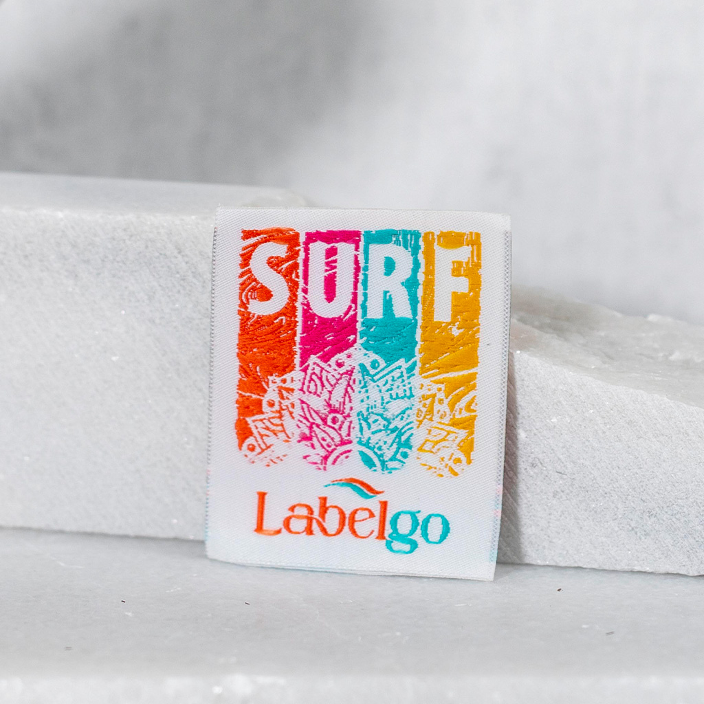 Étiquette tissée blanche avec inscription SURF colorée et palmier.