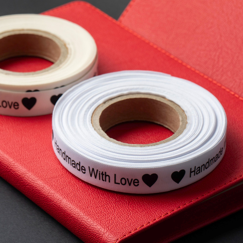 Deux rouleaux d'étiquettes en satin blanc imprimées avec du texte noir sur fond rouge.